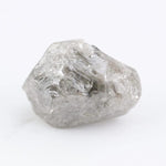 A rough, raw diamond held between metal tweezers against a clean white background.