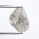 A rough, raw diamond held between metal tweezers against a clean white background.