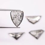 Four salt and pepper lab grown diamonds in shield, trillion, and geometric fancy cuts with natural grey inclusions, displayed on white background as loose ethical conflict-free stones for custom jewelry.