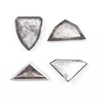 Four salt and pepper lab grown diamonds in shield, trillion, and geometric fancy cuts with natural grey inclusions, displayed on white background as loose ethical conflict-free stones for custom jewelry.