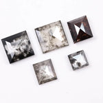 Five square step-cut lab grown diamonds with pyramid-style faceting and visible natural inclusions displayed on a white background, featuring clear, salt and pepper, and champagne tones.