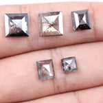 Five square step-cut lab grown diamonds with pyramid-style faceting and visible natural inclusions displayed on a white background, featuring clear, salt and pepper, and champagne tones.