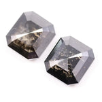 Pair of emerald cut salt and pepper lab grown diamonds with black and white inclusions in geometric step cut, shown loose on white background.