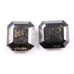 Pair of emerald cut salt and pepper lab grown diamonds with black and white inclusions in geometric step cut, shown loose on white background.
