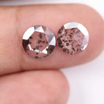 Two round brilliant cut lab grown diamonds with black galaxy-style inclusions on white background, faceted loose stones for custom fine jewelry.