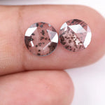 Two round brilliant cut lab grown diamonds with black galaxy-style inclusions on white background, faceted loose stones for custom fine jewelry.