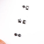 Six natural black diamonds in geometric cuts including star, kite, emerald rectangle, pentagon, and round brilliant shapes displayed on white background.