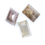 Three natural diamonds including a pink included fancy cut diamond, a golden brown heavily included diamond, and a clear step cut rectangular natural diamond displayed on a white background.