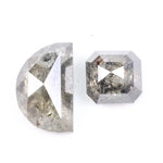 Pair of natural salt and pepper diamonds featuring a half moon rose cut and an octagonal step cut, both with visible grey and black inclusions and a rustic translucent appearance on a white background.