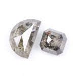 Pair of natural salt and pepper diamonds featuring a half moon rose cut and an octagonal step cut, both with visible grey and black inclusions and a rustic translucent appearance on a white background.