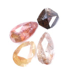 Collection of natural fancy color diamonds including pink, yellow, champagne and cognac loose diamonds with faceted cuts displayed on white background for fine jewelry and gemstone collecting.