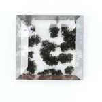 Clear lab-grown diamond with striking black natural-style inclusions inside a polished rectangular crystal, showcasing a unique modern gemstone aesthetic
