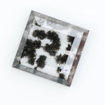 Clear lab-grown diamond with striking black natural-style inclusions inside a polished rectangular crystal, showcasing a unique modern gemstone aesthetic