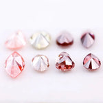 Eight faceted lab grown colored diamonds in pear, oval, and marquise cuts featuring fancy pink, yellow, and deep red tones arranged on a white background.
