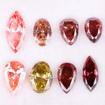 Eight faceted lab grown colored diamonds in pear, oval, and marquise cuts featuring fancy pink, yellow, and deep red tones arranged on a white background.