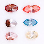 Six fancy color lab grown diamonds on white background including yellow oval cut, blue marquise cut, pink marquise cut, peach pear cut, deep red pear cut, and red oval cut brilliant stones for custom jewelry design.