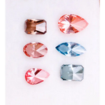 Six fancy color lab grown diamonds displayed on a white background, including pear, marquise, emerald and oval cuts in vibrant pink, blue and cognac tones, precision faceted for fine jewelry settings.