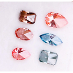 Six fancy color lab grown diamonds displayed on a white background, including pear, marquise, emerald and oval cuts in vibrant pink, blue and cognac tones, precision faceted for fine jewelry settings.