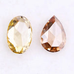 Two lab grown diamonds displayed on white background, including a fancy light yellow oval cut diamond labeled 1 and a champagne pear shaped diamond labeled 2, sustainably created loose stones for engagement rings.