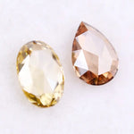 Two lab grown diamonds displayed on white background, including a fancy light yellow oval cut diamond labeled 1 and a champagne pear shaped diamond labeled 2, sustainably created loose stones for engagement rings.