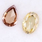 Two lab grown diamonds displayed on white background, including a fancy light yellow oval cut diamond labeled 1 and a champagne pear shaped diamond labeled 2, sustainably created loose stones for engagement rings.