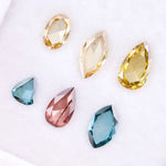 Six lab grown colored diamonds displayed on white background featuring pear, marquise and oval cuts in fancy yellow, champagne, blue and pink shades, ideal for custom engagement rings and fine jewelry settings.