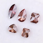 Five lab grown fancy color diamonds in red and cognac tones featuring pear, emerald, marquise, and trillion cuts displayed on a white background, loose sustainable gemstones for custom fine jewelry.