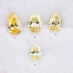 Four fancy yellow lab grown diamonds in pear and oval brilliant cuts displayed on white background, showcasing vivid yellow color, high clarity, and precision faceting.