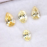 Four fancy yellow lab grown diamonds in pear and oval brilliant cuts displayed on white background, showcasing vivid yellow color, high clarity, and precision faceting.