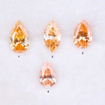 Four fancy colored lab grown diamonds in pear and marquise cuts, featuring vibrant orange and soft peach tones, displayed on a white background as loose sustainable gemstones.