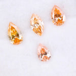 Four fancy colored lab grown diamonds in pear and marquise cuts, featuring vibrant orange and soft peach tones, displayed on a white background as loose sustainable gemstones.