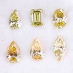 Six fancy yellow lab grown diamonds in pear, emerald, oval, and marquise cuts displayed on a white background, showcasing brilliant sparkle and canary color tones.