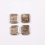 Four emerald-cut champagne lab grown diamonds with visible salt and pepper style inclusions, faceted step-cut stones in warm brown tones on white background