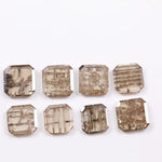 Eight emerald cut lab grown diamonds in champagne tones featuring visible natural-style inclusions and geometric internal patterns, arranged on a white background for fine jewelry selection.