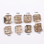 Eight emerald cut lab grown diamonds in champagne tones featuring visible natural-style inclusions and geometric internal patterns, arranged on a white background for fine jewelry selection.