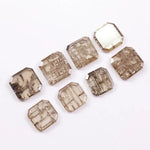 Eight emerald cut lab grown diamonds in champagne tones featuring visible natural-style inclusions and geometric internal patterns, arranged on a white background for fine jewelry selection.