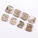 Eight emerald cut lab grown diamonds in champagne tones featuring visible natural-style inclusions and geometric internal patterns, arranged on a white background for fine jewelry selection.