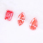Three lab grown pink diamonds displayed on a white background, including a pear cut, marquise cut, and emerald cut fancy vivid pink loose diamonds for custom fine jewelry and engagement rings.