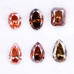 Six fancy colored lab grown diamonds in pink, peach, and cognac tones featuring emerald cut, oval cut, and pear cut shapes displayed on a white background, ethical CVD loose stones for custom fine jewelry.