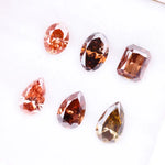 Six fancy colored lab grown diamonds in pink, peach, and cognac tones featuring emerald cut, oval cut, and pear cut shapes displayed on a white background, ethical CVD loose stones for custom fine jewelry.