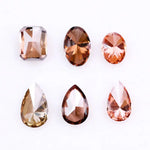 Six fancy colored lab grown diamonds in pink, peach, and cognac tones featuring emerald cut, oval cut, and pear cut shapes displayed on a white background, ethical CVD loose stones for custom fine jewelry.