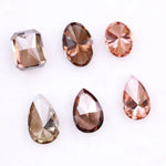 Six fancy colored lab grown diamonds in pink, peach, and cognac tones featuring emerald cut, oval cut, and pear cut shapes displayed on a white background, ethical CVD loose stones for custom fine jewelry.