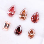 Six lab grown fancy colored diamonds in pink, blush, champagne and deep rose tones featuring pear, oval and emerald cuts displayed on a white background for fine jewelry design.