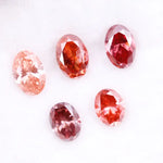 Five oval cut pink lab grown diamonds displayed on a white background, ranging in color from light blush pink to deep vivid rose and red tones, shown for color comparison and gemstone selection.
