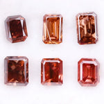 Six lab grown fancy orange pink emerald cut diamonds displayed on a white background, rectangular step cut loose grown diamonds in various reddish peach shades for engagement rings and fine jewelry.