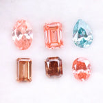 Lab grown fancy pink, peach, cognac and blue diamonds in oval, emerald and pear cuts displayed on white background, sustainable CVD created gemstones for fine jewelry.