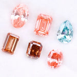 Lab grown fancy pink, peach, cognac and blue diamonds in oval, emerald and pear cuts displayed on white background, sustainable CVD created gemstones for fine jewelry.