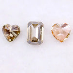 Three lab grown fancy color diamonds including pink heart cut, champagne emerald cut, and yellow heart shape loose diamonds for engagement ring and custom jewelry making