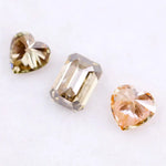 Three lab grown fancy color diamonds including pink heart cut, champagne emerald cut, and yellow heart shape loose diamonds for engagement ring and custom jewelry making