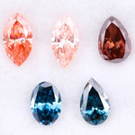 Collection of fancy color lab grown diamonds including pink marquise cut, light peach marquise, brown pear shape, blue oval cut and blue pear cut loose diamonds displayed on white background